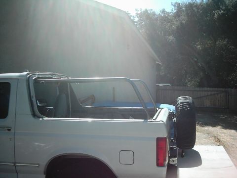 1978 Ford Bronco - Side view of a white SUV with a roll cage and spare tire. The year is not discernible from the image.