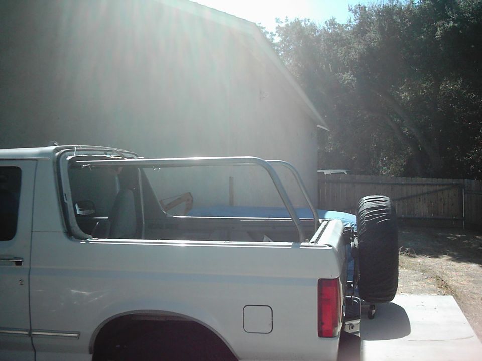White SUV, possibly a Bronco, with a roll cage installed and spare tire mounted on the rear. The vehicle appears to be undergoing some work