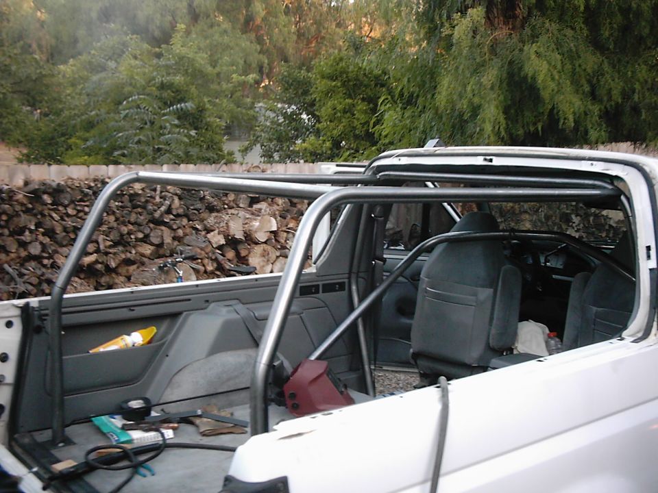 White SUV interior with a metal roll cage, dark seats, and a pile of firewood in the background