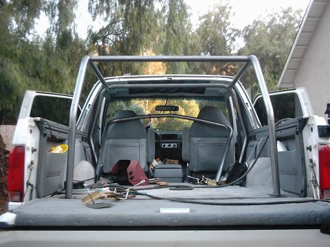 1978 Ford Bronco - The interior of a white SUV is visible, a custom roll cage and grey seats.
