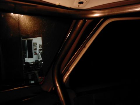 1978 Ford Bronco - Interior view of a vehicle's roll cage and window frame, with a reflection showing framed pictures on a wall.