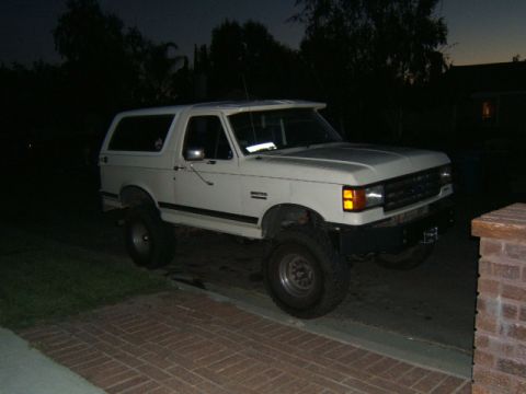 1988 Ford Bronco - This lifted SUV is parked on a brick driveway with a dark sky and trees in the background.