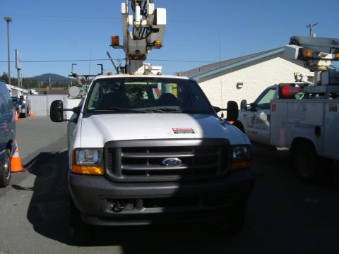 1993 Ford Bronco - A white Ford F-Series truck with a utility boom is parked in front of a building, with another utility truck to its right.