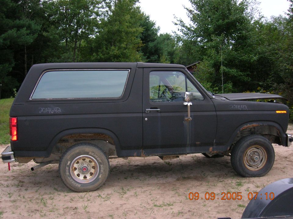 Black 1980s Ford Bronco, side view, hood up, flat tire, rust on wheel wells