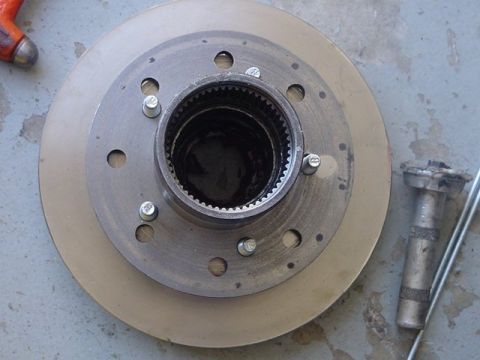 1971 Ford Bronco - Close-up of a vehicle's brake rotor and hub assembly, with a tool nearby on a grey surface.