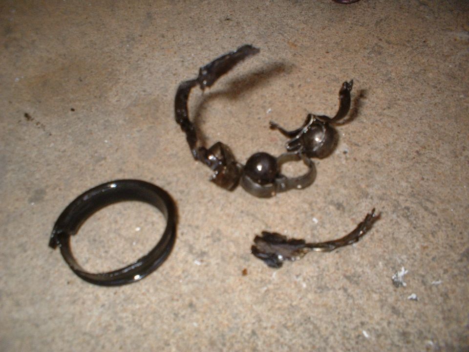 Broken rubber and metal parts, a spring clip and ball studs, scattered on concrete