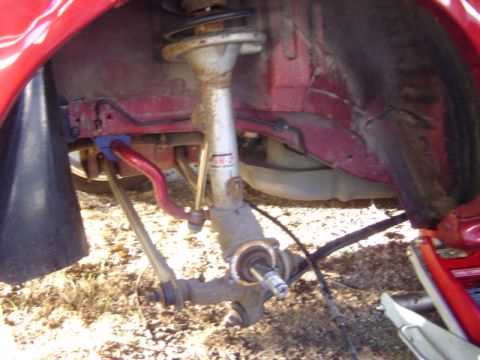 1998 Ford Taurus - Close-up view of a red car's suspension system, showing the shock absorber and sway bar.