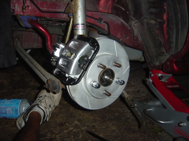 close-up of a car's front brake rotor and caliper assembly, with a red sway bar visible above