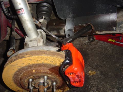 1998 Ford Taurus - Close-up of an aftermarket orange racing brake caliper on a vehicle's suspension.