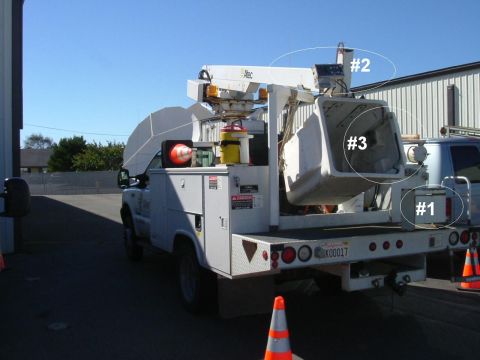 1993 Ford Bronco - A utility truck is parked outside a building, equipped with a large bucket lift and storage boxes on its bed.