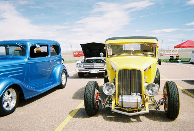 Yellow hot rod car with exposed engine and chrome accents, parked on asphalt