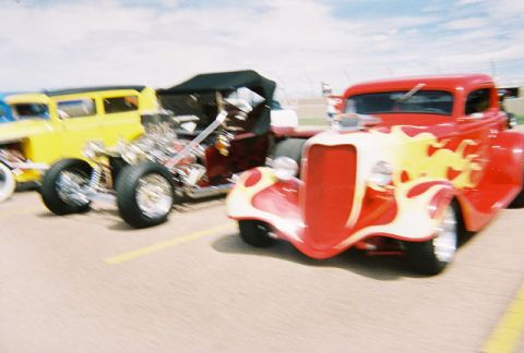 1972 Ford Ranchero - A red hot rod with custom yellow flames is parked alongside a yellow vehicle.