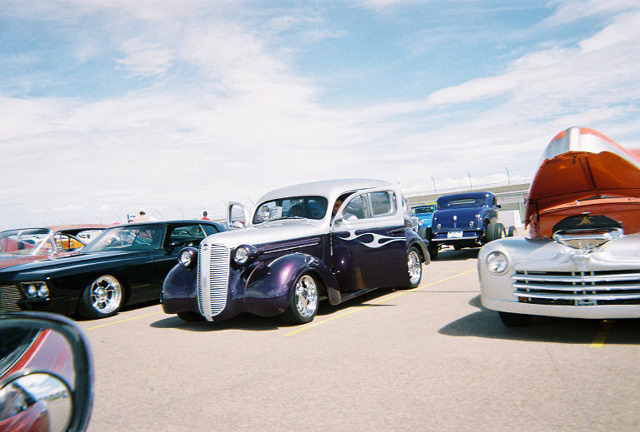 Purple and silver hot rod with flame decals, hood open on a silver truck in the foreground