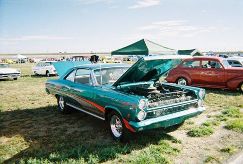 1972 Ford Ranchero - A teal 1966 Mercury Comet coupe with its hood open is displayed at an outdoor car show.
