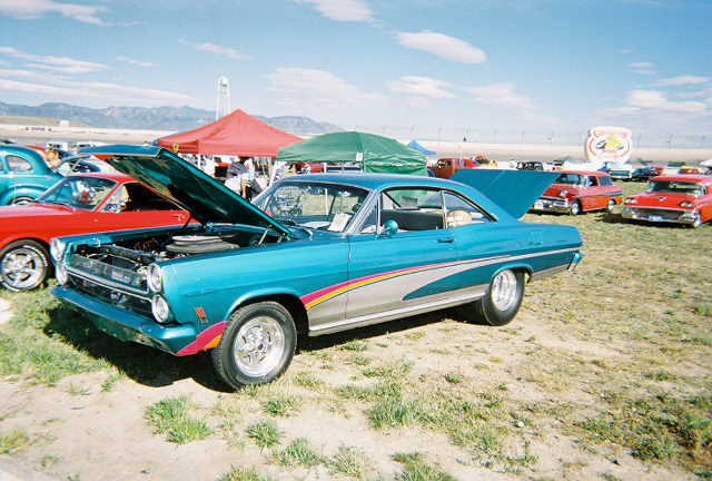 1966 Ford Falcon with hood open at car show. Other classic cars and tents in background