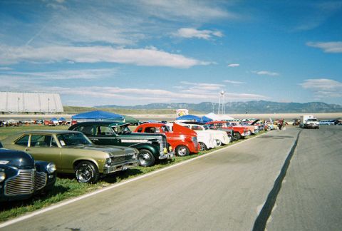 1972 Ford Ranchero - A line of vintage automobiles are parked on a grassy area next to a paved track on a sunny day.