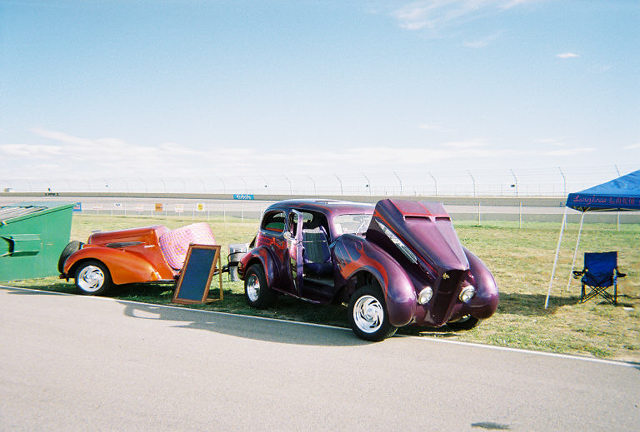 Purple hot rod with flames and open hood, parked next to an orange trailer with a pink blanket
