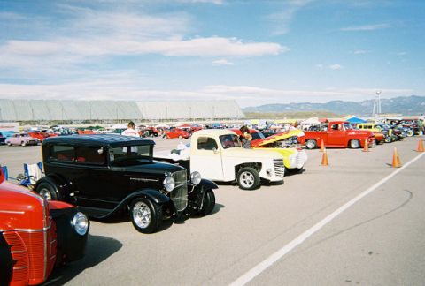 1972 Ford Ranchero - A black sedan is parked at an outdoor car show, with many other vehicles visible under a bright blue sky.