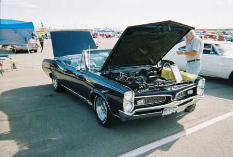 1972 Ford Ranchero - A man inspects the engine of a classic convertible at an outdoor car show.