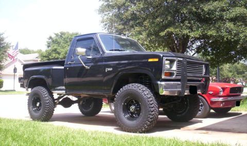 1984 Ford F-150 - Lifted black Ford F-150 pickup truck is parked next to a red Ford Mustang.