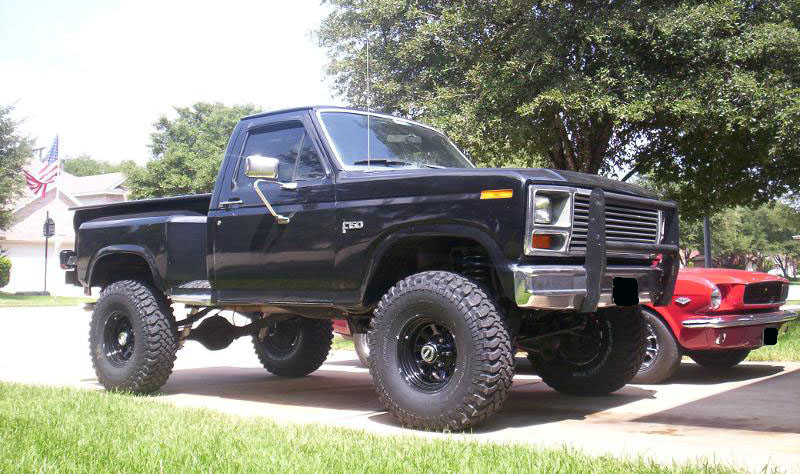 Lifted black 1980s Ford F-150 stepside pickup beside red Mustang in driveway