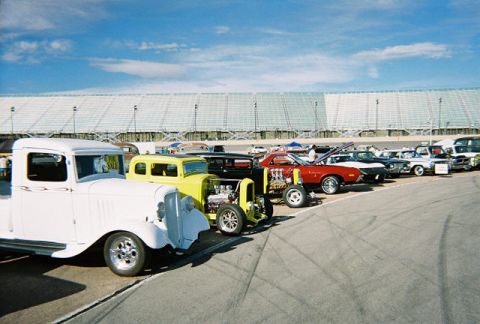1972 Ford Ranchero - A variety of vintage vehicles are lined up at what appears to be a car show or race track event.