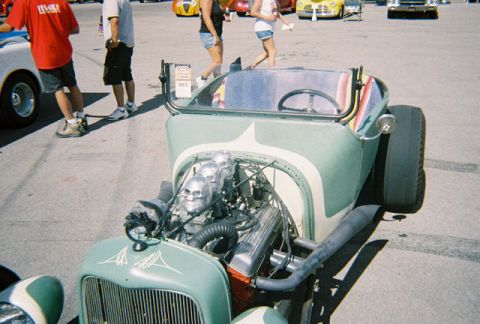 1972 Ford Ranchero - A custom hot rod with a unique skull-adorned engine is displayed at an outdoor event.
