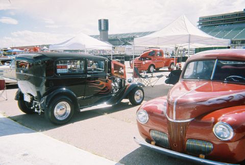 1972 Ford Ranchero - A black hot rod with flame decals is parked at an outdoor event, with other vehicles and tents visible.