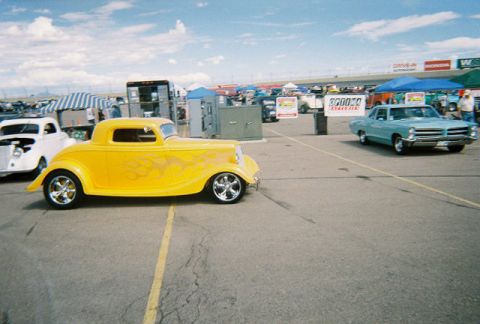 1972 Ford Ranchero - A yellow hot rod coupe with flame decals is parked on asphalt next to other vehicles and tents.