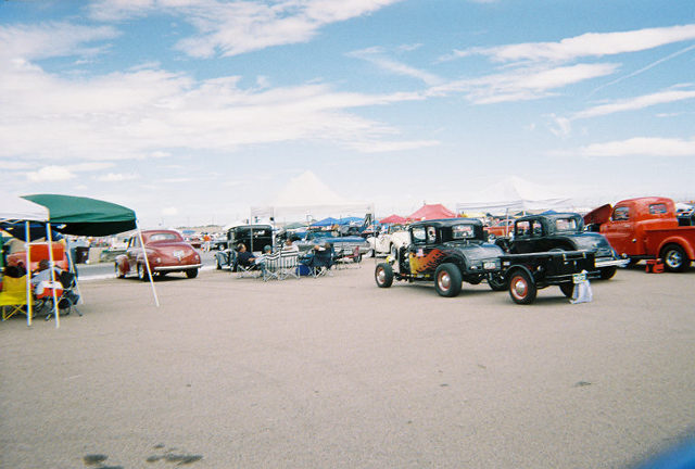 Several hot rod trucks and cars parked on asphalt under a cloudy sky