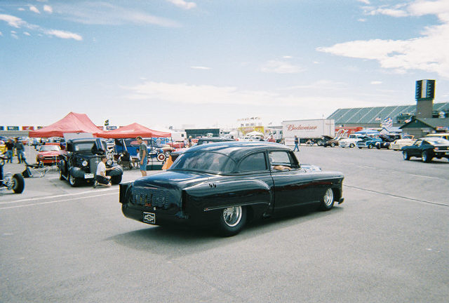 Black classic car with lowered suspension and chrome wheels, viewed from the rear