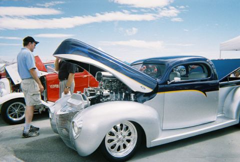 1972 Ford Ranchero - A custom pickup truck with its hood open is displayed at an outdoor event, with another vehicle visible behind it.
