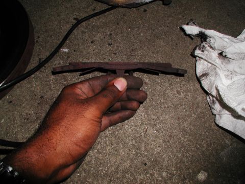 1992 Ford Taurus - A hand holds a worn brake pad, showing the metal backing plate and friction material, next to a dirty paper towel and part of a brake rotor.