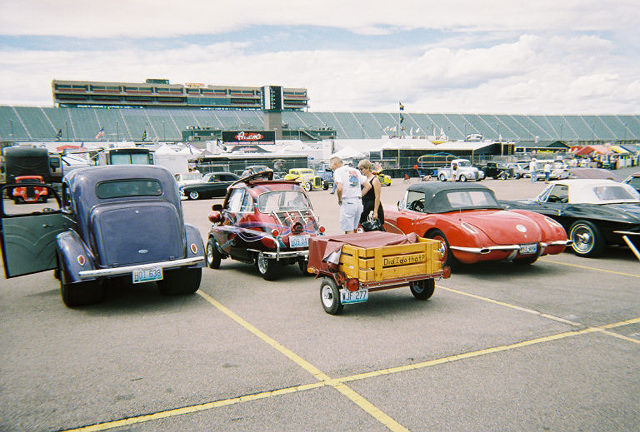 Blue sedan with open driver's door, rear view, parked on asphalt
