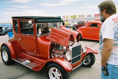 1972 Ford Ranchero - A red 1920s coupe hot rod is displayed with its hood open at an outdoor event.