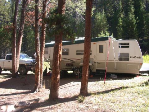 1994 Ford Bronco - A pickup truck is parked next to a travel trailer at a campsite.