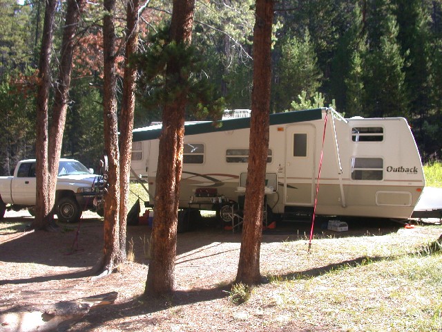 White pickup truck parked next to a travel trailer in a wooded area