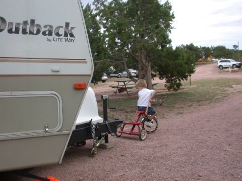 1994 Ford Bronco - A young boy rides a tricycle near a parked trailer at a campsite.