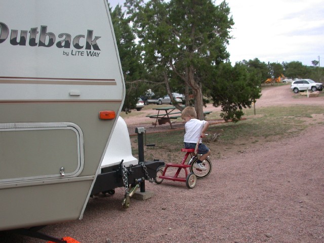 Child on red tricycle near trailer hitch, white SUV in background