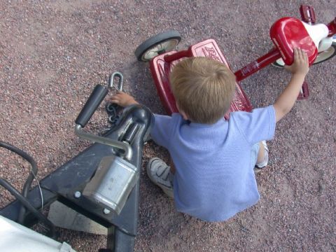 1994 Ford Bronco - A young child interacts with a red tricycle and a trailer hitch assembly on a gravel surface.