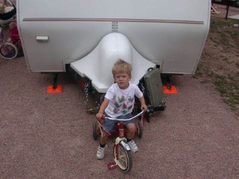 1994 Ford Bronco - A young boy sits on a tricycle, positioned in front of the hitch of a large recreational vehicle.