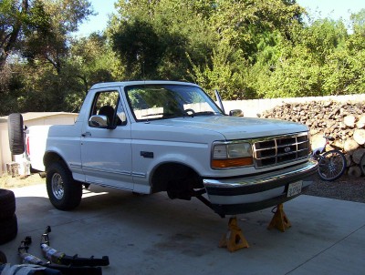 1995 Ford Bronco - White Ford Bronco with its front end elevated on jack stands, showing a spare tire on the back.