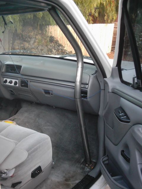 1978 Ford Bronco - The interior of a white truck shows a roll cage installed, with grey seats and dashboard visible.