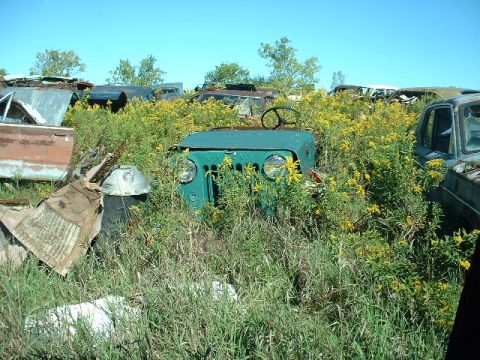 1978 Ford Mustang II - Junkyard scene with an overgrown green Jeep CJ front end and other vehicle parts.