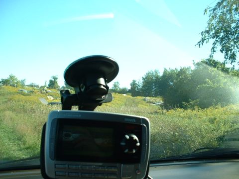 1978 Ford Mustang II - A GPS device is mounted on the dashboard, with a view of a grassy field and trees through the windshield.