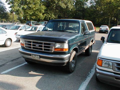 1994 Ford Bronco - A green 1994 Ford Bronco with a white top is parked in a lot next to another vehicle.