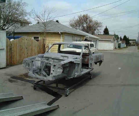 1967 Ford Ranchero - The body of a pickup truck is undergoing restoration, mounted on a stand in a driveway.