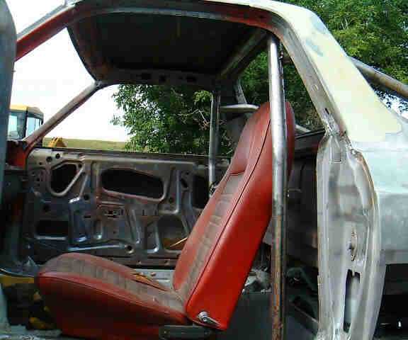 Stripped car interior with red bucket seat, bare metal door, and roll cage tubing.