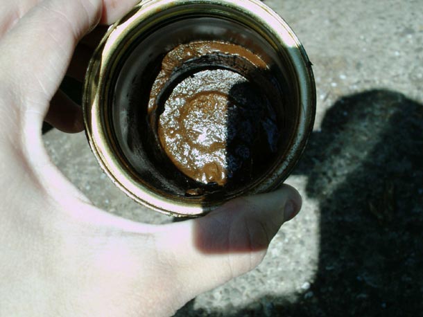 Hand holding used oil filter cut open showing thick dark sludge inside