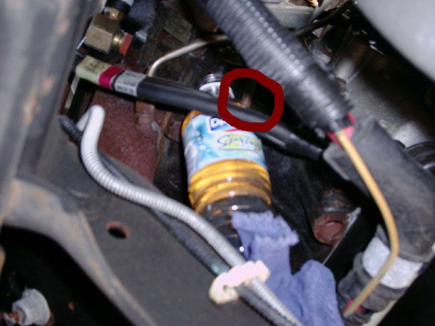 Bottle positioned under a diesel fuel filter drain, with the drain circled in red
